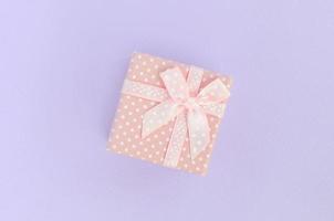 Small pink gift box with ribbon lies on a violet background. Minimalism flat lay top view photo