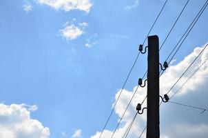 Old wooden electric pole for transmission of wired electricity on a background of a cloudy blue sky. Obsolete method of supplying electricity for later use photo