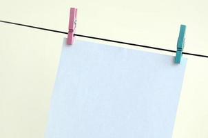 White blank cards on rope, light wall background. Creative reminder, small sheets of paper on old clothespin, memo backdrop photo