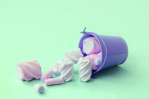 Overturned miniature lilac bucket filled with marshmallow lies on a turquoise pastel background photo