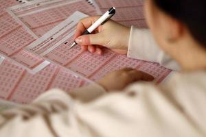 llenando un boleto de lotería. una joven juega a la lotería y sueña con ganar el premio mayor. mano femenina marcando el número en el billete de lotería rojo foto