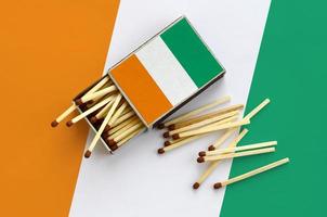 Ivory Coast flag  is shown on an open matchbox, from which several matches fall and lies on a large flag photo