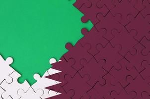 Qatar flag  is depicted on a completed jigsaw puzzle with free green copy space on the left side photo