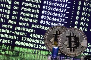 Two bitcoins lies on a videocard surface with background of screen display of cryptocurrency mining by using the GPUs photo