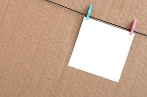 White blank card on rope on a brown cardboard background. Creative reminder, small sheet of paper on wooden clothespin, memo backdrop photo