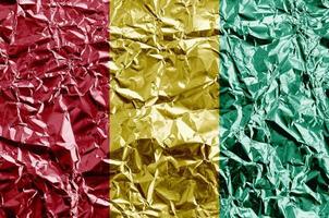 Guinea flag depicted in paint colors on shiny crumpled aluminium foil closeup. Textured banner on rough background photo