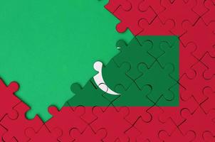 Maldives flag  is depicted on a completed jigsaw puzzle with free green copy space on the left side photo