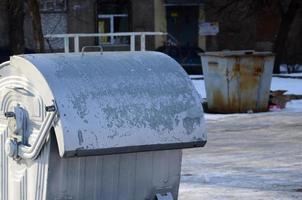 A silver garbage container stands near residential buildings in winter photo