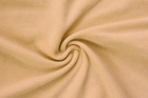 The blanket of furry orange fleece fabric. A background of light orange soft plush fleece material with a lot of relief folds photo