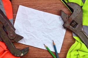 A crumpled sheet of paper with two pencils surrounded by green and orange working uniforms and adjustable wrenches photo