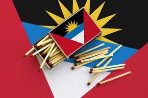 Antigua and Barbuda flag  is shown on an open matchbox, from which several matches fall and lies on a large flag photo