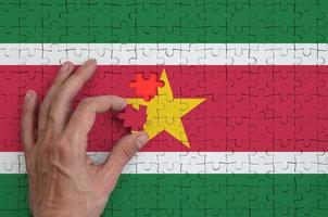 Suriname flag  is depicted on a puzzle, which the man's hand completes to fold photo