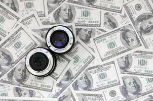 Two photographic lenses lie on the background of a lot of dollar bills. Space for text photo