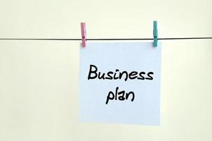 Business plan. Note is written on a white sticker that hangs with a clothespin on a rope on a background of beige wall photo