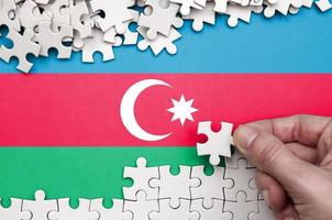 Azerbaijan flag  is depicted on a table on which the human hand folds a puzzle of white color photo