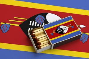 Swaziland flag  is shown in an open matchbox, which is filled with matches and lies on a large flag photo