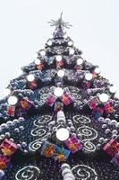 A fragment of a huge Christmas tree with many ornaments, gift boxes and luminous lamps. Photo of a decorated Christmas tree close-up with copy space