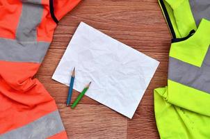 una hoja de papel arrugada con dos lápices rodeada de uniformes de trabajo verdes y naranjas foto