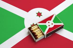 Burundi flag  is shown in an open matchbox, which is filled with matches and lies on a large flag photo