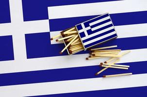 Greece flag  is shown on an open matchbox, from which several matches fall and lies on a large flag photo