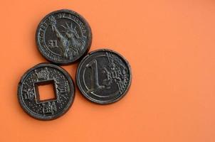 Three chocolate products in the form of Euro, USA and Japan coins lie on an orange plastic background. A model of cash coins in an edible form photo