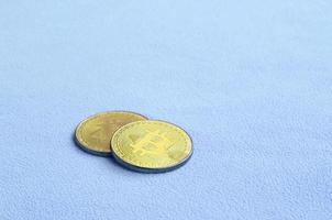 Two golden bitcoins lies on a blanket made of soft and fluffy light blue fleece fabric. Physical visualization of virtual crypto currency photo