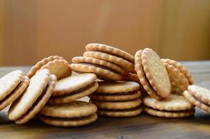 A round sandwich cookie with coconut filling lies in large quantities on a brown wooden surface. Photo of edible treats on a wooden background with copy space