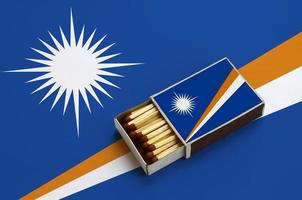 Marshall Islands flag  is shown in an open matchbox, which is filled with matches and lies on a large flag photo