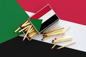 Sudan flag  is shown on an open matchbox, from which several matches fall and lies on a large flag photo