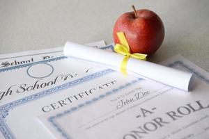 A honor roll recognition, certificate of achievement and high school diploma lies on table with small scroll and red apple. Education documents photo