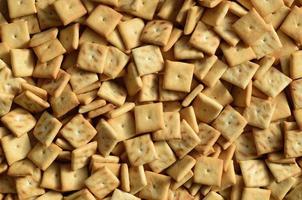 A lot of small cookies are square shaped. A pattern of a yellow salt cracker. Background image with salted pastry photo