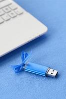 la tarjeta de memoria flash usb azul brillante con un lazo azul se encuentra sobre una manta de tela polar azul claro suave y peluda junto a una computadora portátil blanca. diseño clásico de regalo femenino para una tarjeta de memoria foto