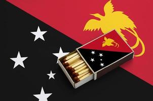Papua New Guinea flag  is shown in an open matchbox, which is filled with matches and lies on a large flag photo