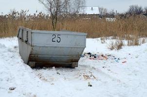 Trash bin at the side of street in winter with lip garbage container winter snow. Metal container for household waste photo