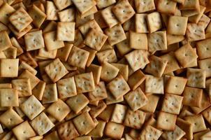 A lot of small cookies are square shaped. A pattern of a yellow salt cracker. Background image with salted pastry photo