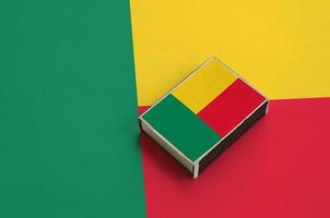 Benin flag  is pictured on a matchbox that lies on a large flag photo