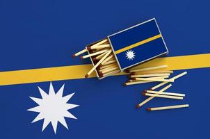 Nauru flag  is shown on an open matchbox, from which several matches fall and lies on a large flag photo