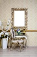 A fragment of a retro interior with a chair and table, on which is a telephone and a vase of flowers. Above the table hangs an empty picture frame for your photo