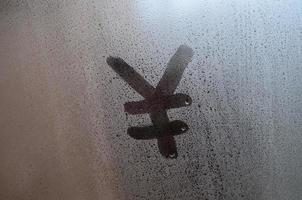 Chinese Yen Symbol is written with a finger on the surface of the misted glass photo