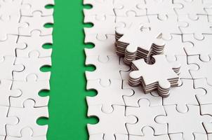 The green path is laid on the platform of a white folded jigsaw puzzle. The missing elements of the puzzle are stacked nearby. Texture image with space for text photo