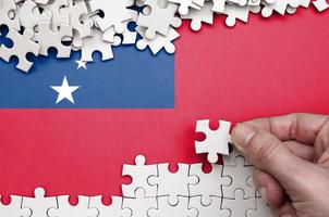 Samoa flag  is depicted on a table on which the human hand folds a puzzle of white color photo