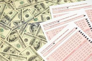 Pink gambling sheets with numbers for marking on big amount of hundred dollar bills. Lottery playing concept or gambling addiction. Close up photo