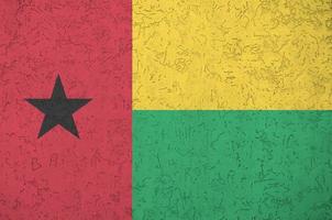 Guinea Bissau flag depicted in bright paint colors on old relief plastering wall. Textured banner on rough background photo