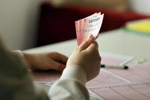 llenando un boleto de lotería. una mujer joven sostiene el billete de lotería con una fila completa de números en el fondo de las hojas en blanco de la lotería. foto
