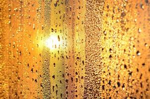 The texture of misted glass with a lot of drops and drips of condensation against the sunlight at dawn. Background image photo