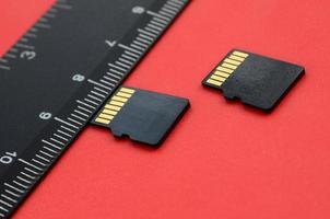 Two small micro SD memory cards lie on a red background next to a black ruler. A small and compact data and information store photo