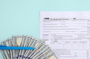 1040 tax form lies near hundred dollar bills and blue pen on a light blue background. US Individual income tax return photo