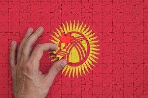 Kyrgyzstan flag  is depicted on a puzzle, which the man's hand completes to fold photo