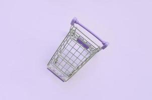 Small shopping cart lies on a violet background. Minimalism flat lay top view photo