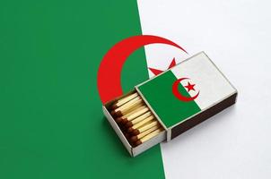 Algeria flag  is shown in an open matchbox, which is filled with matches and lies on a large flag photo